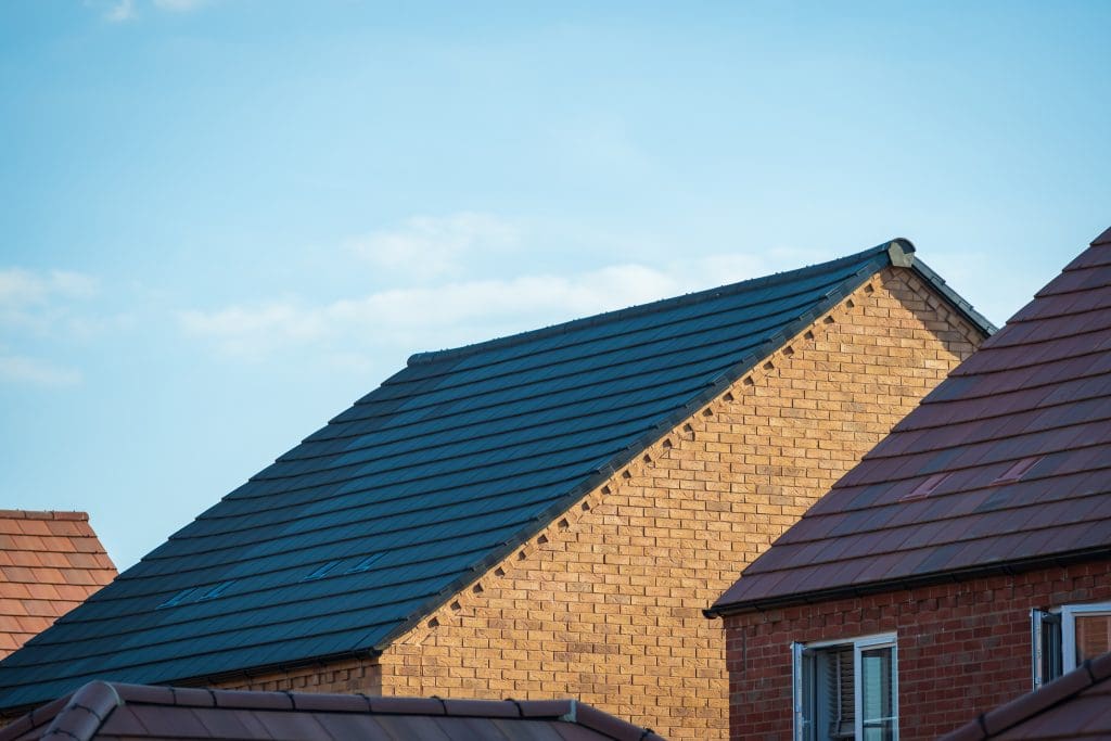 Several modern brick houses with sloped roofs under a clear blue sky, with the main focus on a yellow brick house featuring a dark gray tiled roof.